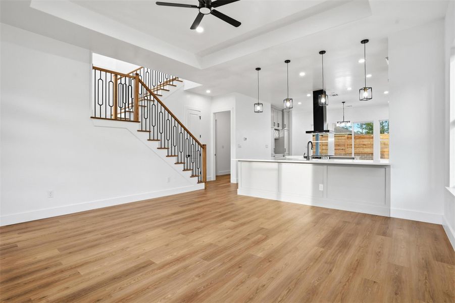 Unfurnished living room featuring a raised ceiling, light wood-style floors, ceiling fan, and recessed lighting