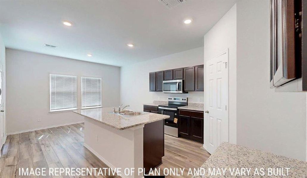 Open-concept kitchen featuring an island with a built-in sink, granite countertops, dark wood cabinetry, and stainless steel appliances