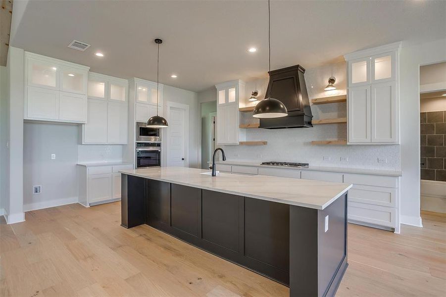 Kitchen with premium range hood, open shelves, visible vents, stainless steel appliances, and a sink Kitchen with premium range hood, open shelves, visible vents, stainless steel appliances, and a sink