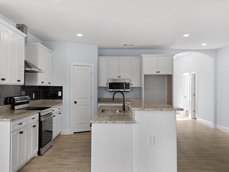 Kitchen with arched walkways, stainless steel appliances, light wood finished floors, recessed lighting, and an island with sink