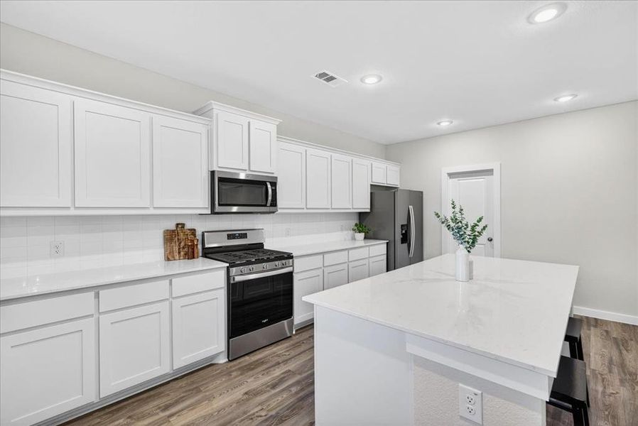 Kitchen featuring stainless steel appliances, a center island, backsplash, white cabinets, and a breakfast bar