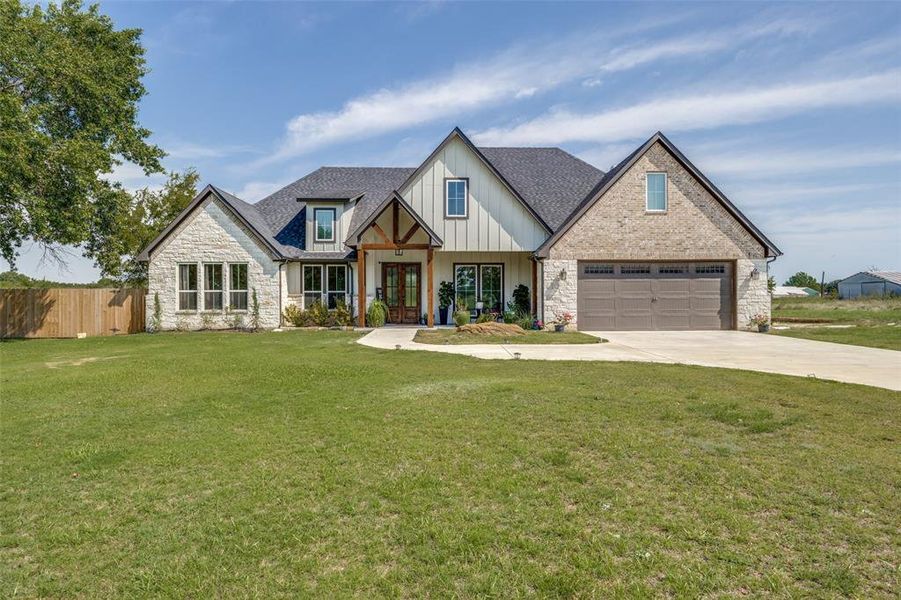 View of front of house with stone siding, a porch, a garage, driveway, and board and batten siding