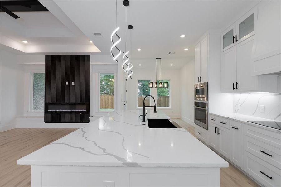 Kitchen featuring pendant lighting, an island with sink, white cabinets, open floor plan, and light wood-style floors