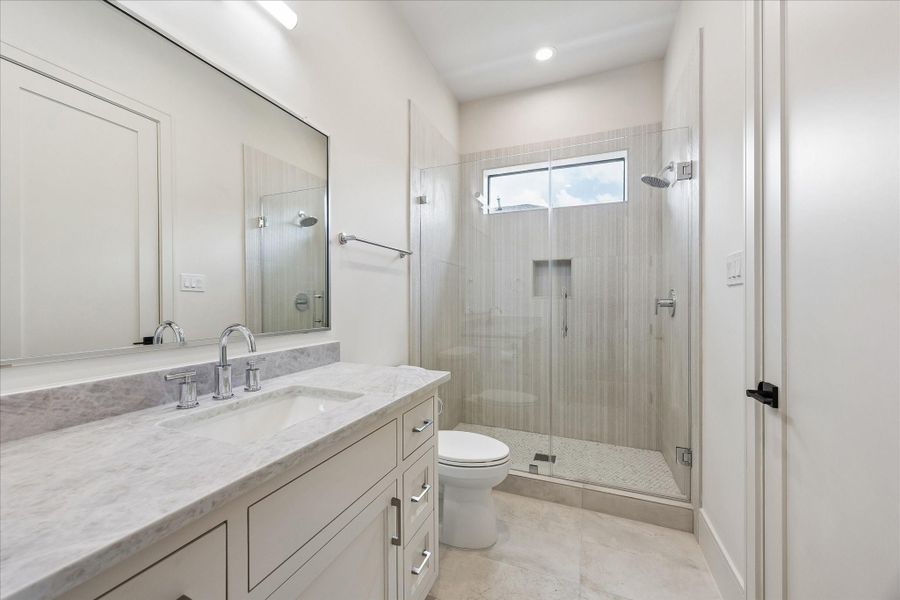 Soft neutral finishes, a quartz vanity, and a frameless glass shower create a timeless ensuite bath. Full height tile, a built in shower niche, and transom window add both style and natural light.