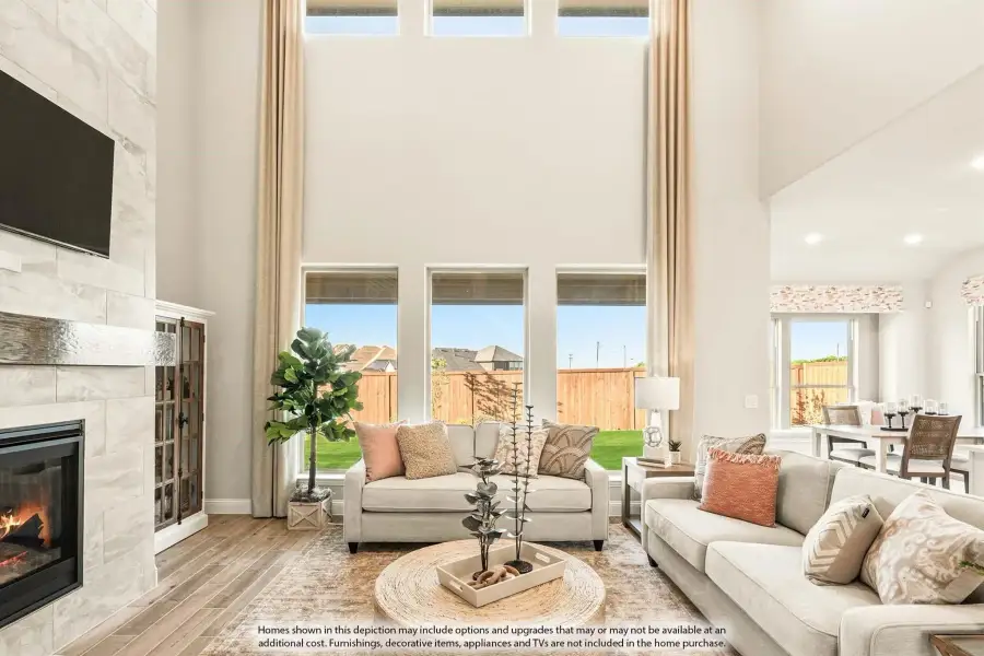 Living room with two-story ceiling, tile fireplace, large windows, and neutral sofas on hardwood floors