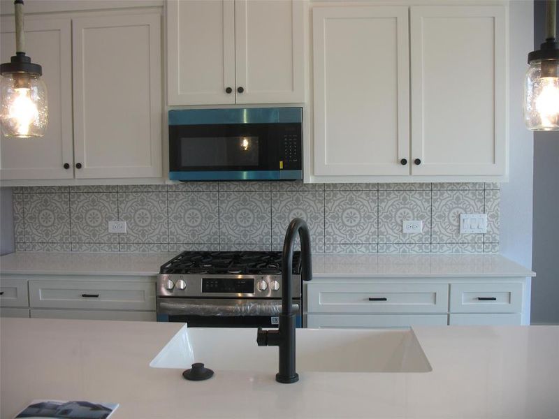 Kitchen featuring hanging light fixtures, white cabinets, stainless steel appliances, decorative backsplash, and light stone countertops
