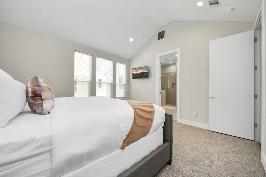 The primary suite feels noticeably open thanks to its vaulted ceiling, multiple windows, and direct connection to the private bath.