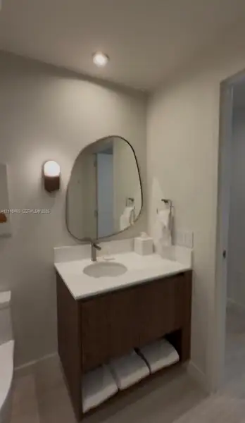 Wood-finish floating vanity with a stone countertop, integrated undermount sink, asymmetrical wall mirror, and modern wall-mounted sconce