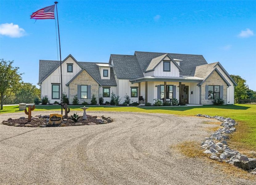Modern inspired farmhouse with board and batten siding, stone siding, covered porch, roof with shingles, and circular driveway Modern inspired farmhouse with board and batten siding, stone siding, covered porch, roof with shingles, and circular driveway