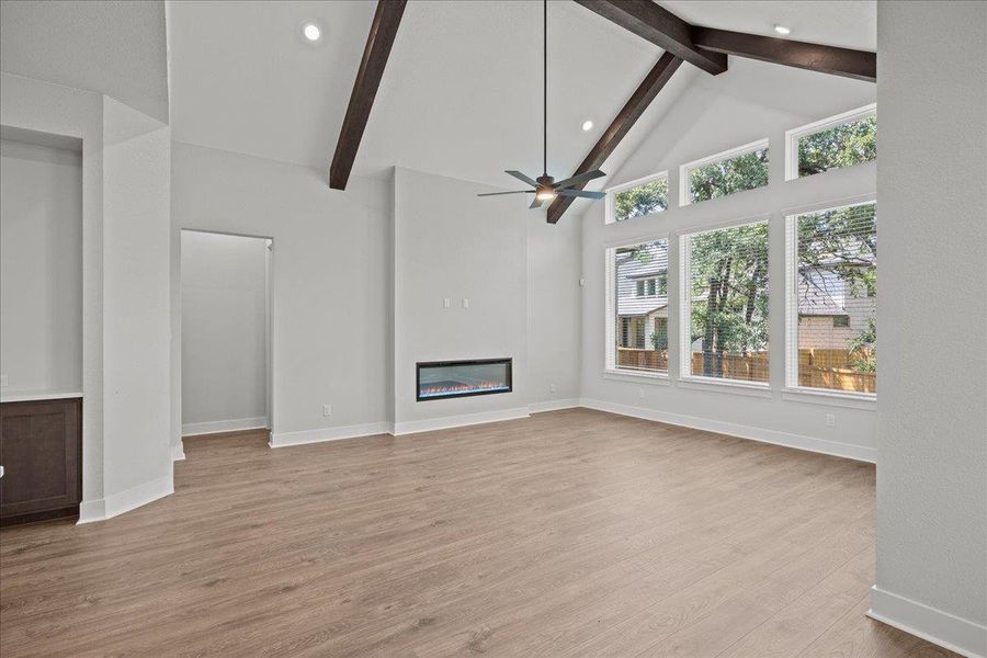 Unfurnished living room with beam ceiling, a glass covered fireplace, light wood-type flooring, high vaulted ceiling, and recessed lighting Unfurnished living room with beam ceiling, a glass covered fireplace, light wood-type flooring, high vaulted ceiling, and recessed lighting