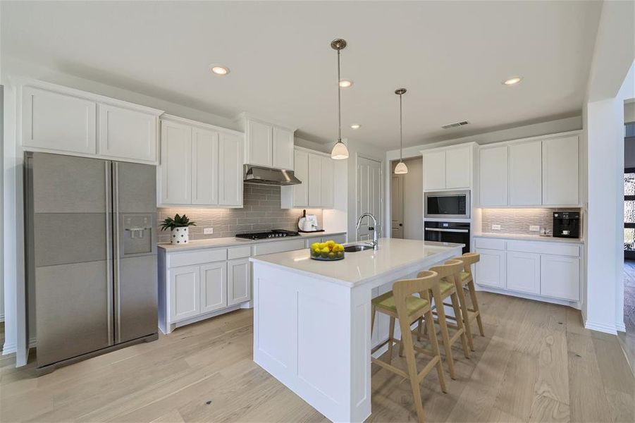 Virtually Staged Photo - Kitchen with backsplash, appliances with stainless steel finishes, light hardwood / wood-style floors, and wall chimney range hood