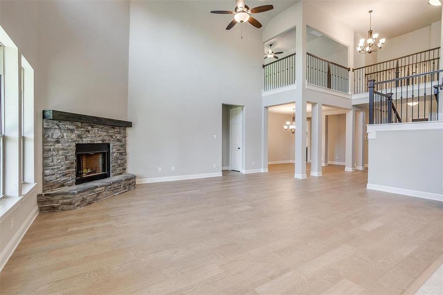 Unfurnished living room with a towering ceiling, a stone fireplace, ceiling fan with notable chandelier, and light hardwood / wood-style floors