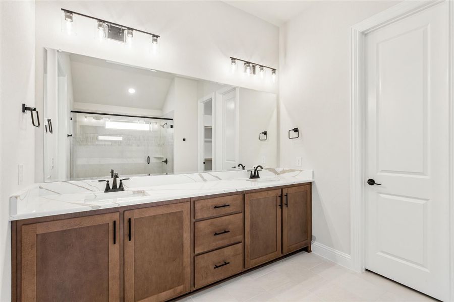 Bathroom with double vanity, wood cabinets, white quartz countertop, and large mirror with overhead lighting