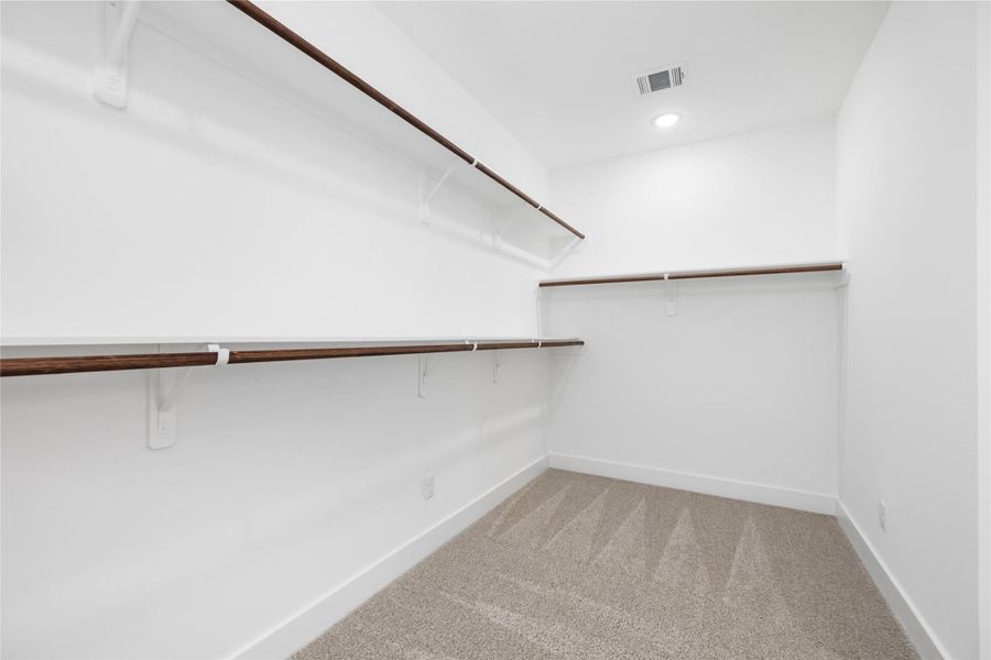 This massive walk-in closet is a true highlight, featuring clean white walls and multiple white shelves for a bright, airy feel. The plush carpeted floor adds warmth and comfort, while abundant overhead lighting ensures the entire space is well-lit, providing the perfect setting for organization and easy access to your wardrobe.