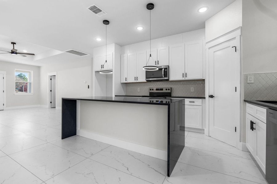 White cabinets, appliances with stainless steel finishes, decorative light fixtures, decorative backsplash