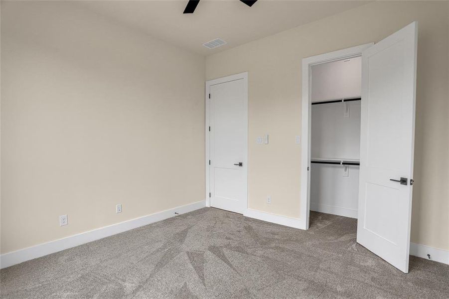 Unfurnished bedroom featuring carpet flooring, ceiling fan, a walk in closet, and a closet Unfurnished bedroom featuring carpet flooring, ceiling fan, a walk in closet, and a closet