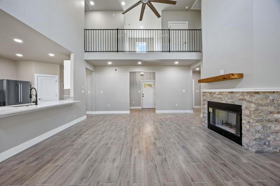 Unfurnished living room featuring a stone fireplace, baseboards, recessed lighting, a ceiling fan, and wood finished floors Unfurnished living room featuring a stone fireplace, baseboards, recessed lighting, a ceiling fan, and wood finished floors