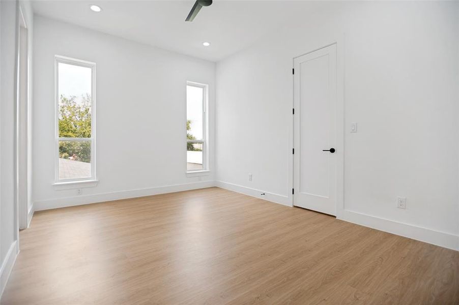 Bright room featuring wood-finish flooring, two vertical windows, a vaulted ceiling, recessed lighting, and a modern ceiling fan