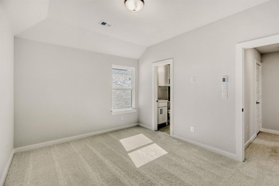 Unfurnished bedroom with vaulted ceiling, light carpet, and ensuite bathroom