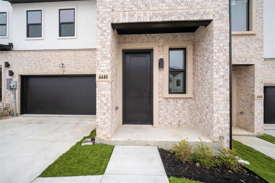 Doorway to property with a garage, brick siding, and driveway