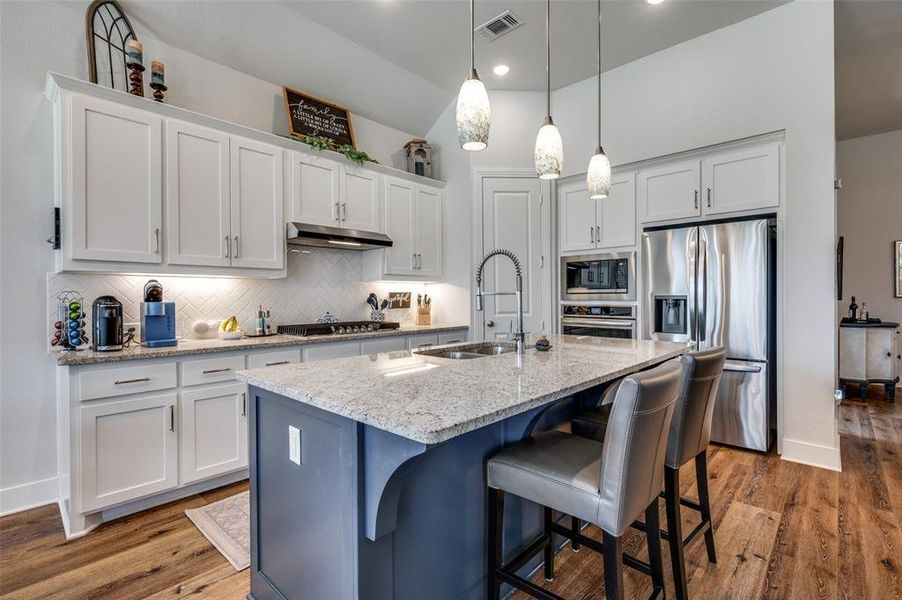 Kitchen featuring stainless steel appliances, light stone countertops, an island with sink, decorative light fixtures, and a kitchen breakfast bar