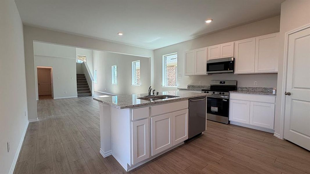 Modern kitchen featuring white cabinetry, stainless steel appliances, granite countertops, and a center island with sink Modern kitchen featuring white cabinetry, stainless steel appliances, granite countertops, and a center island with sink
