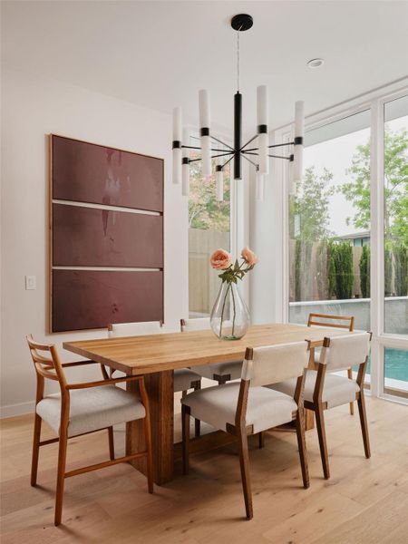 Dining space featuring a modern black and white chandelier, light wood-finish flooring, and large windows