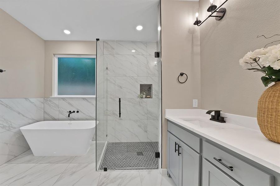 Contemporary bathroom featuring a freestanding tub, glass-enclosed shower with mosaic tile floor, and a double vanity with light gray cabinetry Contemporary bathroom featuring a freestanding tub, glass-enclosed shower with mosaic tile floor, and a double vanity with light gray cabinetry