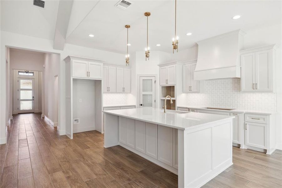 Kitchen with premium range hood, a kitchen island with sink, sink, and white cabinets