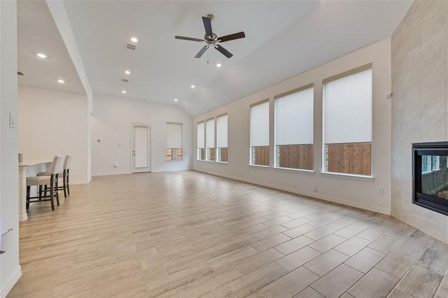 Unfurnished living room with ceiling fan, lofted ceiling, a tile fireplace, recessed lighting, and light wood-type flooring Unfurnished living room with ceiling fan, lofted ceiling, a tile fireplace, recessed lighting, and light wood-type flooring