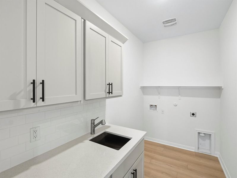 Functional utility room featuring upper cabinetry, a sink, and connections for laundry appliances. Functional utility room featuring upper cabinetry, a sink, and connections for laundry appliances.