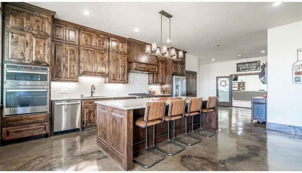 Kitchen featuring stainless steel appliances, a kitchen island, a sink, concrete flooring, and backsplash Kitchen featuring stainless steel appliances, a kitchen island, a sink, concrete flooring, and backsplash