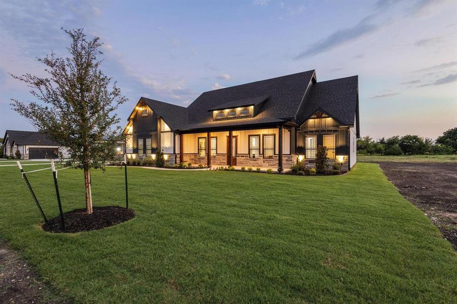 Modern farmhouse style home featuring board and batten siding, covered porch, a lawn, and roof with shingles