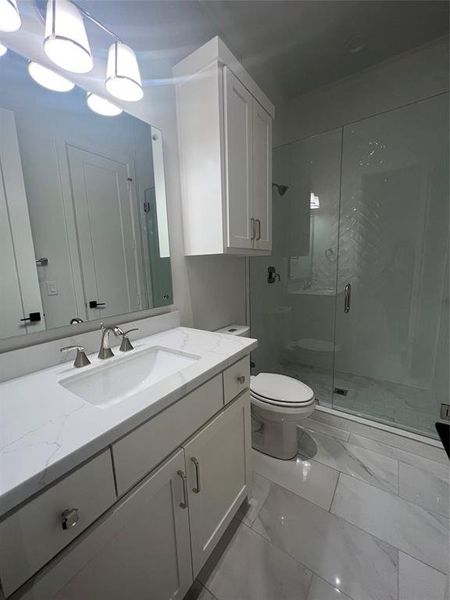 Bathroom with vanity with extensive cabinet space, a shower with shower door, toilet, and tile floors