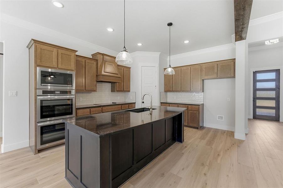 Kitchen featuring light wood-style floors, a kitchen island with sink, dark stone countertops, stainless steel appliances, and wood finish cabinets