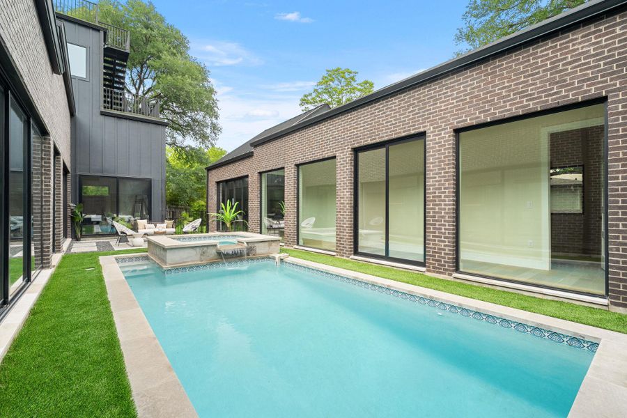 Outdoor swimming pool with integrated spa and waterfall feature, surrounded by green lawn and stone coping