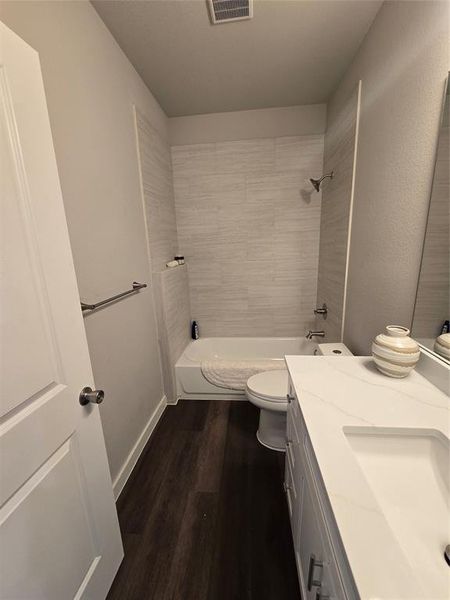 Full bathroom with hardwood / wood-style flooring, tiled shower / bath combo, vanity, and toilet