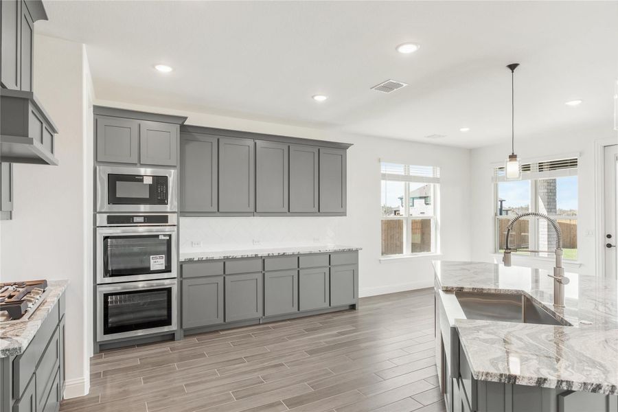 Kitchen with gray shaker cabinets, stainless steel double oven, microwave, and marble countertops on wood-look tile floors Kitchen with gray shaker cabinets, stainless steel double oven, microwave, and marble countertops on wood-look tile floors