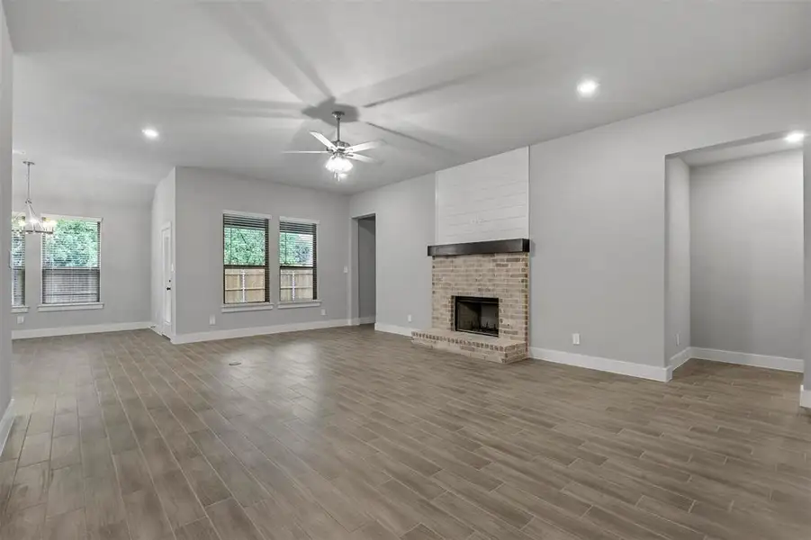 Unfurnished living room featuring a fireplace, light hardwood / wood-style floors, and ceiling fan with notable chandelier