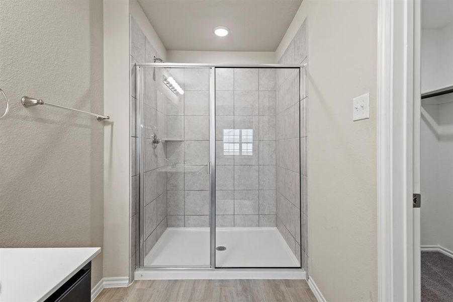 Bathroom with a textured wall, vanity, a shower stall, and light wood finished floors Bathroom with a textured wall, vanity, a shower stall, and light wood finished floors