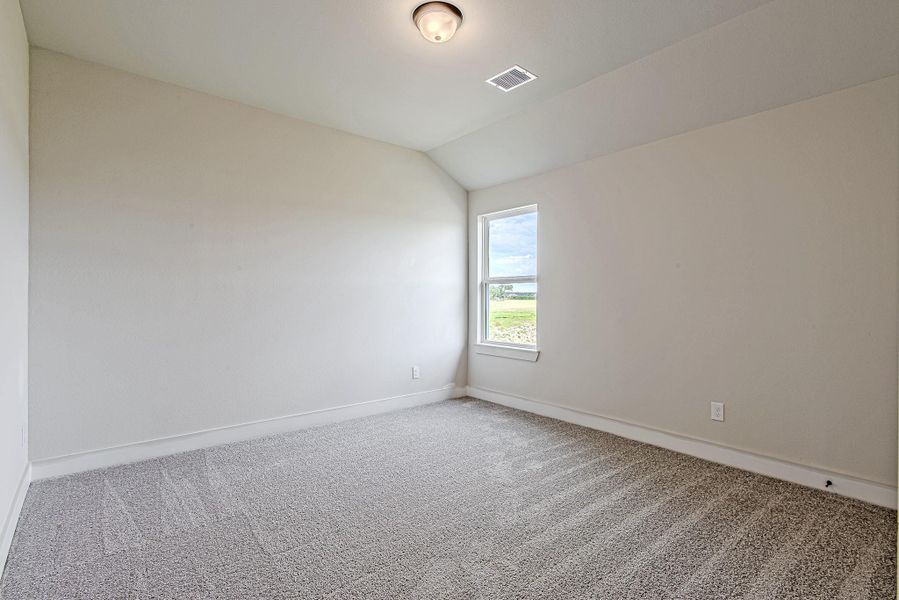 Spacious secondary bedroom featuring a vaulted ceiling, fresh carpeting, and serene views of the lush green space beyond.