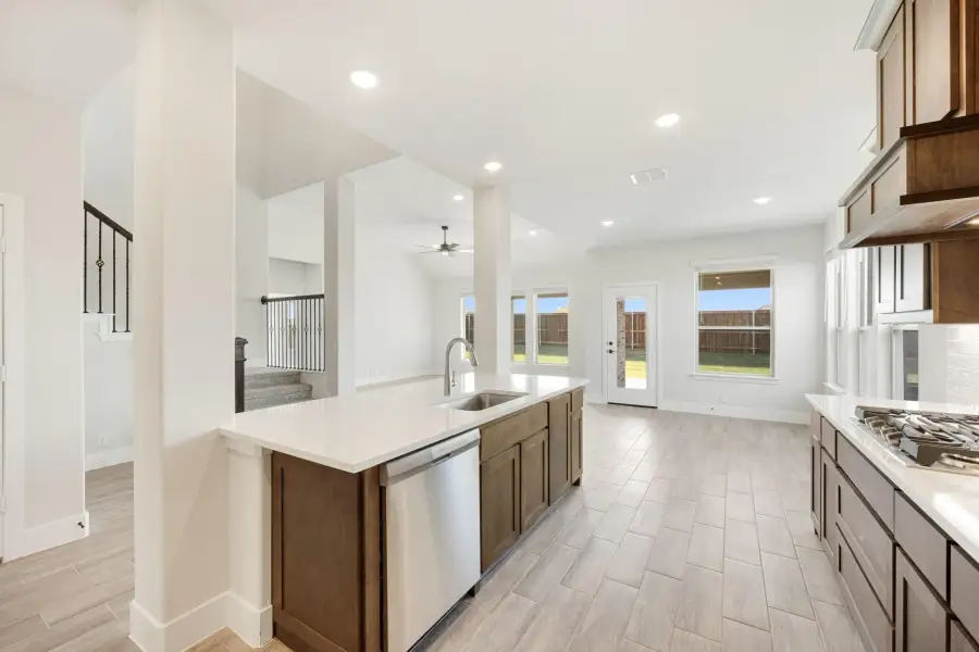 Kitchen with dark wood cabinets, center island with sink, stainless dishwasher, and white quartz countertops open to living area