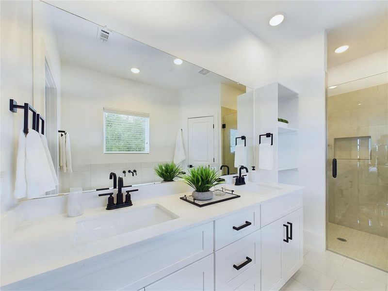 Private ensuite featuring a double vanity with ample storage, sleek black fixtures, a large mirror, and a freestanding tub near a window with a pleasant view.