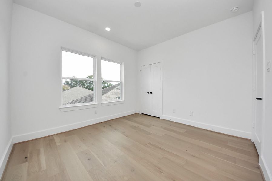 A bright, versatile room with light wood flooring, crisp white walls, and a double window that fills the space with natural light. A double-door closet makes it ideal as a bedroom, guest room, or home office.