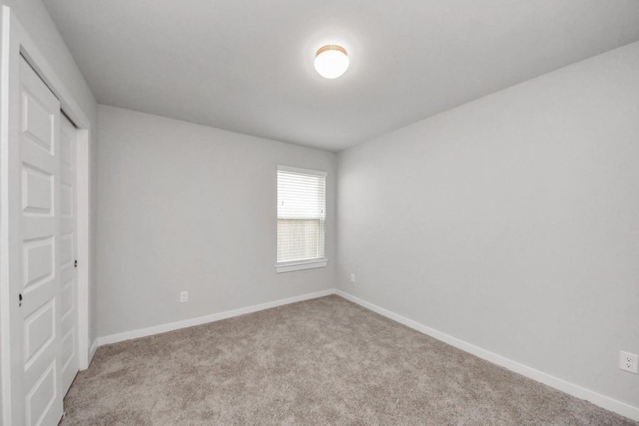 Comfortable secondary bedroom with soft carpeting, a window bringing in natural light, and convenient access to the shared hallway bathroom.