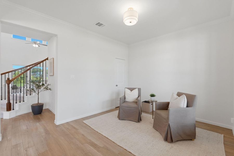 This photo shows a bright, open room with light wood tile flooring and neutral walls. It features two comfortable armchairs on a cozy area rug, with a small table and plant. An adjacent staircase with wooden railing leads to another level, enhancing the inviting atmosphere.