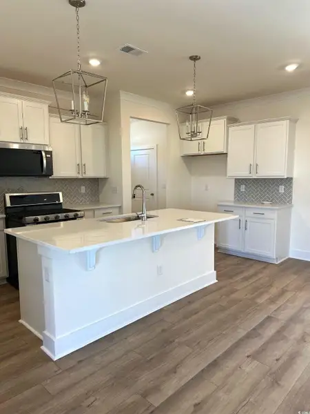Kitchen featuring tasteful backsplash, white cabinets, ornamental molding, stainless steel appliances, and dark wood-style floors