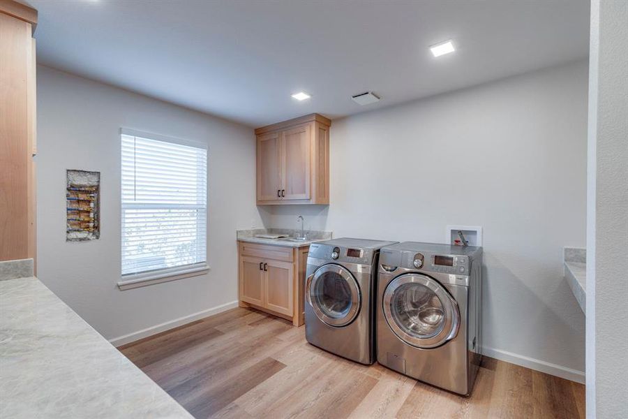 Laundry room featuring cabinets, separate washer and dryer, sink, and light wood-type flooring