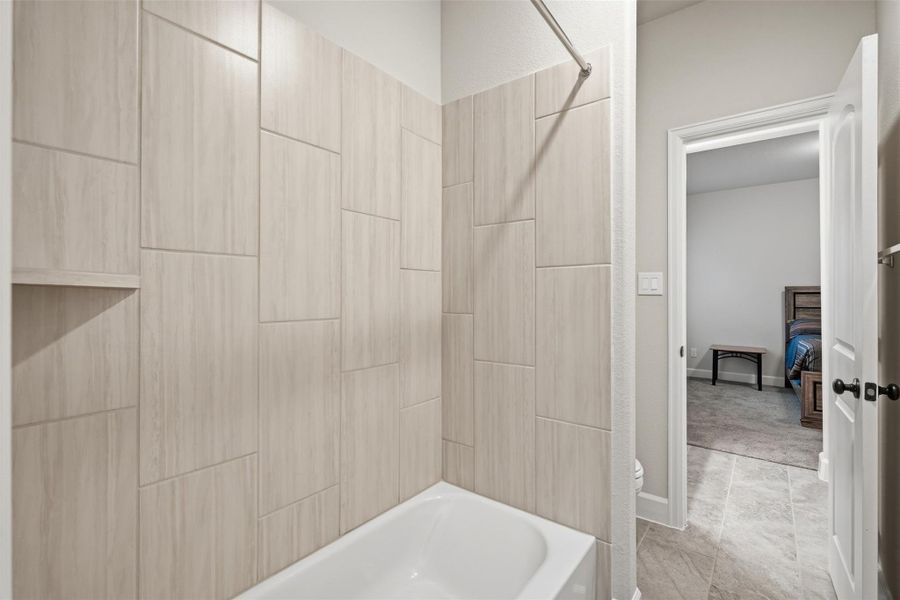 This photo shows a modern bathroom with a tiled shower and bathtub combo. The light-colored tiles create a clean, spacious feel. The room opens to a carpeted bedroom, adding convenience and accessibility. This photo shows a modern bathroom with a tiled shower and bathtub combo. The light-colored tiles create a clean, spacious feel. The room opens to a carpeted bedroom, adding convenience and accessibility.