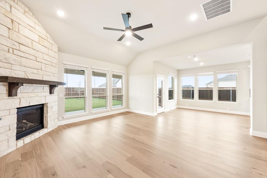 Open living room with stone fireplace, hardwood floors, vaulted ceiling, and ceiling fan